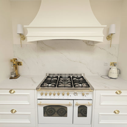 A white gas stove and oven with gold knobs, set into a white marble countertop and backsplash, beneath a white range hood with wall-mounted gold sconces- with Lofra White and Brass 90cm range cooker 