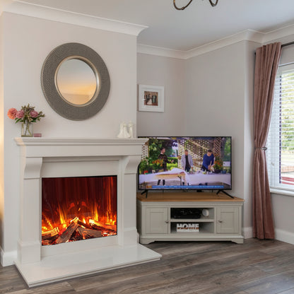 A cream / white fireplace insert with a glowing Electric Iconic 750 electric fire log fire, set in a living room next to a TV stand and window.