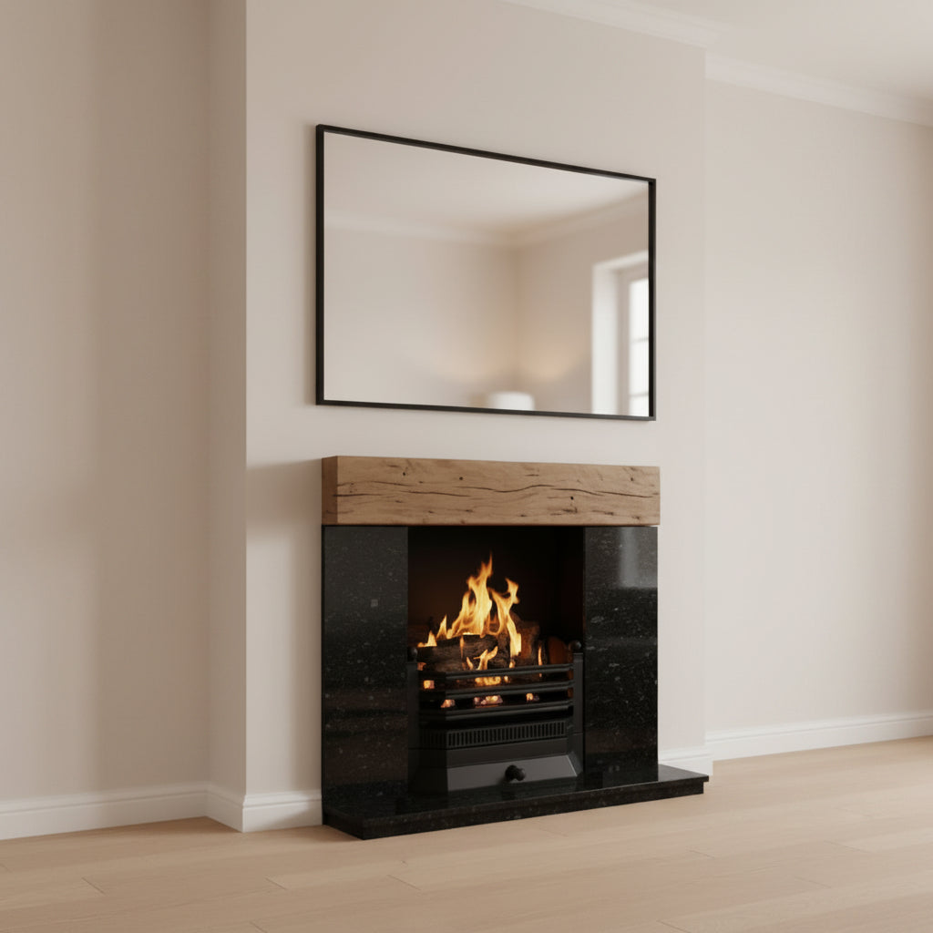 A modern gas fireplace insert with a black marble surround and a light wood mantel, shown lit with orange flames. A large black-framed mirror hangs on the wall above it in a clean, minimalist room with beige walls and light wood flooring.