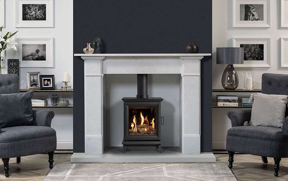 Gazco Sheraton Gas Stove in a Living room with a fireplace, gray chairs, and framed pictures on the wall.
