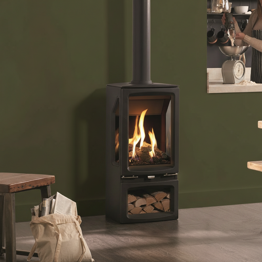 A black Gazco Vogue Midi T Midline CF 3-Sided Conventional Flue Gas Stove with a realistic log effect fuel bed, situated in a room with a wooden floor and a bookshelf, reflecting a fire in the stove.