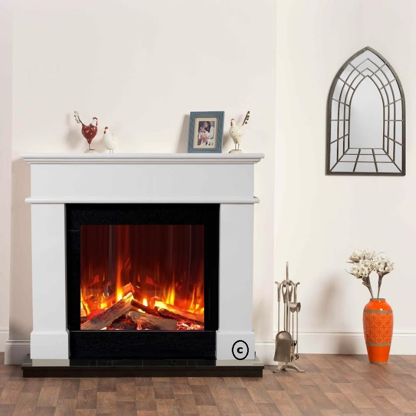 A white electric fireplace with a glowing faux Iconic 750 electric wood fire, set in a styled room with a wood floor, wall art, and decorative accessories.