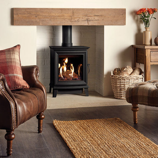 Gazco Chesterfield Gas Stove in Living room with a fireplace, brown armchair, and decorative items.