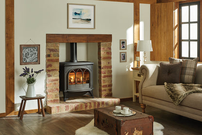 A conventional Gazco Huntingdon 40 clear glass gas stove with a glass front and a log flame effect, installed in a fireplace alcove with a framed picture and mirror above, in a room with a leather sofa and a fur throw.
