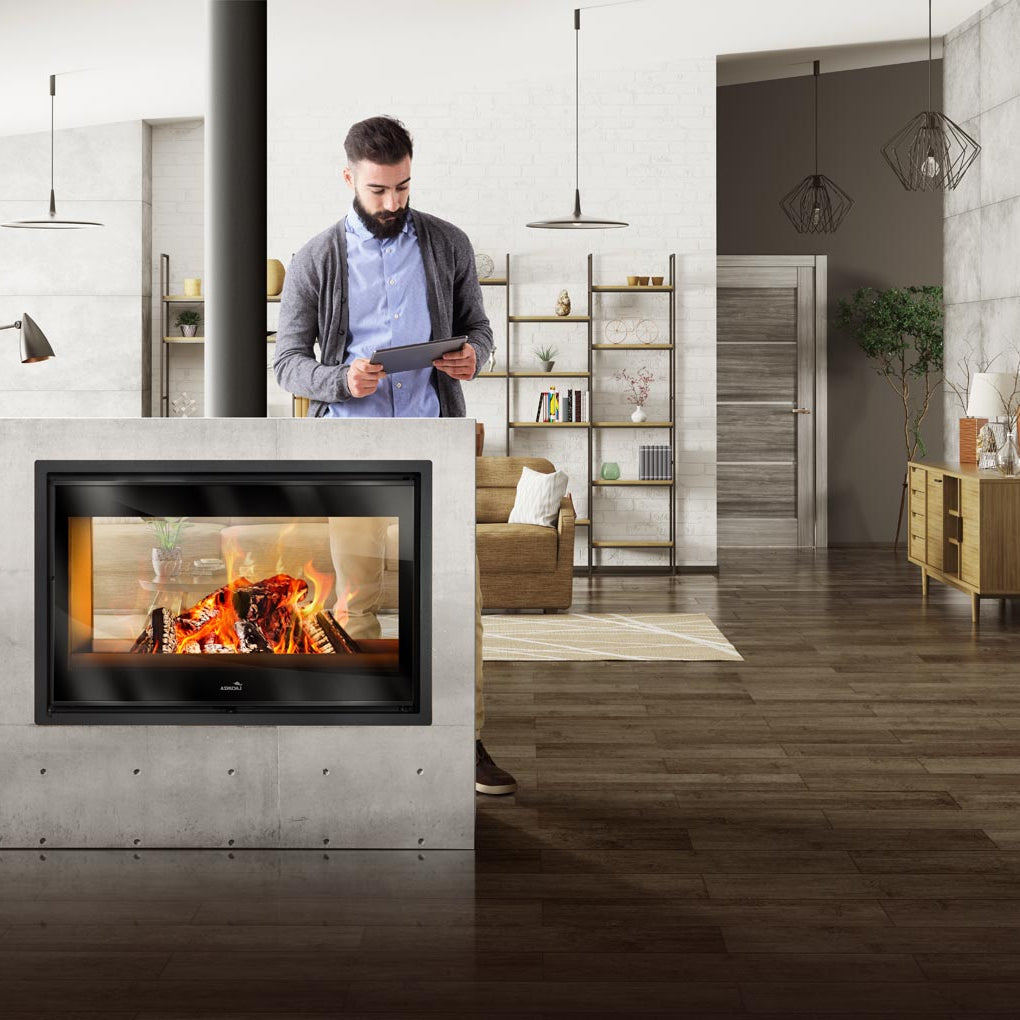 Man using a tablet in a modern living room with a Lacunza Nickel Double Sided Wood Burning Stove Range for Ireland