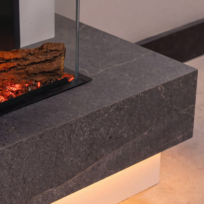 A modern floating fireplace mantel made of dark gray stone, featuring a glass wind guard and a faux log with glowing embers inside.