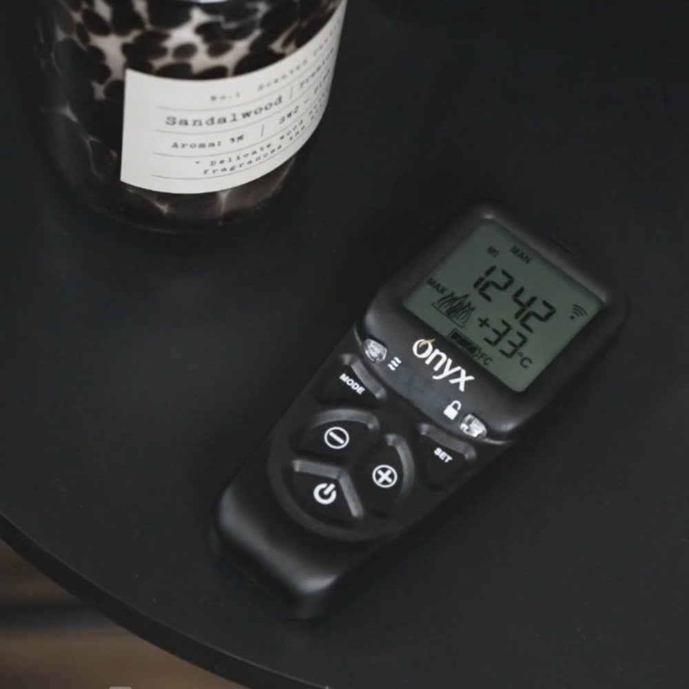 Digital Thermostatic Onyx Remote Control Handset on a dark surface with a leopard print candle in the background from the Onyx Liv 3 Gas Stove High Efficiency Gas Stove Ireland Contemporary Log Effect Gas Stove