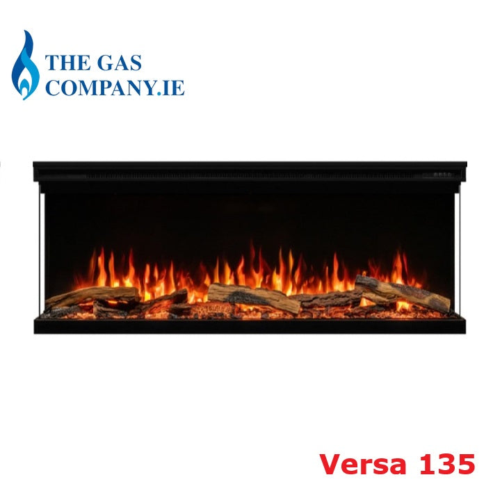 A black linear electric Atmos Fire FX Versa fireplace with a realistic orange and yellow flame effect over faux logs, shown on a white background with 'THE GAS COMPANY.IE' logo at the top left and 'Versa 135' text at the bottom right.