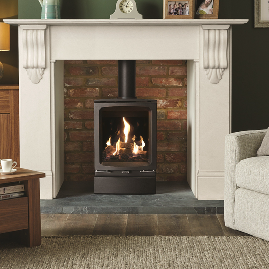 A black Gazco Vogue Midi gas stove with a realistic log effect fuel bed, installed in a contemporary style interior with a decorative brick wall and a polished stainless steel insert, alongside a programmable thermostat.