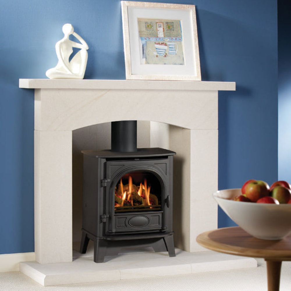 Gazco Stockton 5 Balanced Flue Gas in Fireplace with a lit stove against a blue wall, featuring a framed picture and sculpture on the mantel.