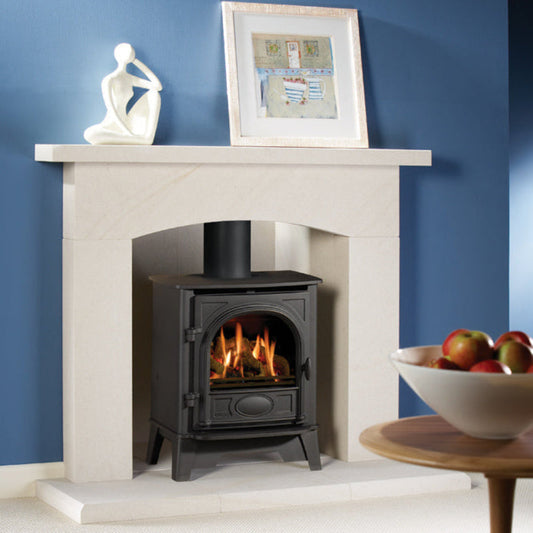 Gazco Stockton 5 Balanced Flue Gas in Fireplace with a lit stove against a blue wall, featuring a framed picture and sculpture on the mantel.