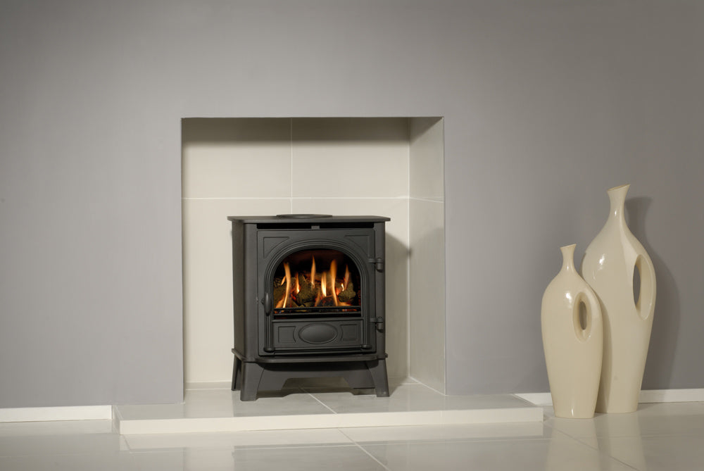 Gazco Stockton 5 Balanced Flue Gas Stove in Modern fireplace with a lit fire, white mantel, and decorative vases against a gray wall.