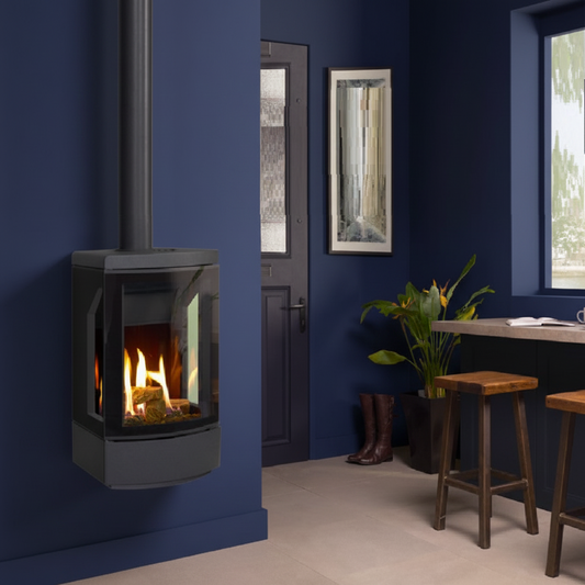 A wall-mounted Gazco Loft Balanced Flue gas stove with a black glass front and visible flames, installed in a room with stools and a mirror in a warm navy blue toned room.