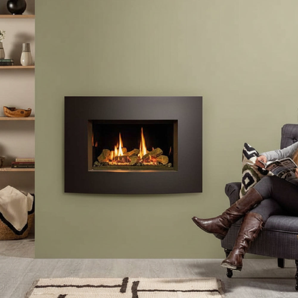 Person sitting on a couch in front of a modern fireplace with a green wall with a Gazco Riva2 600 Conventional Flue Log Effect Gas Fire with Verve XS Graphite Frame